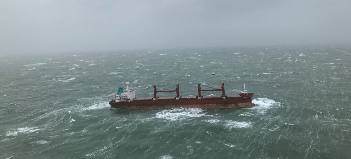 Een groot vrachtschip drijft stuurloos op een stormachtige zee.