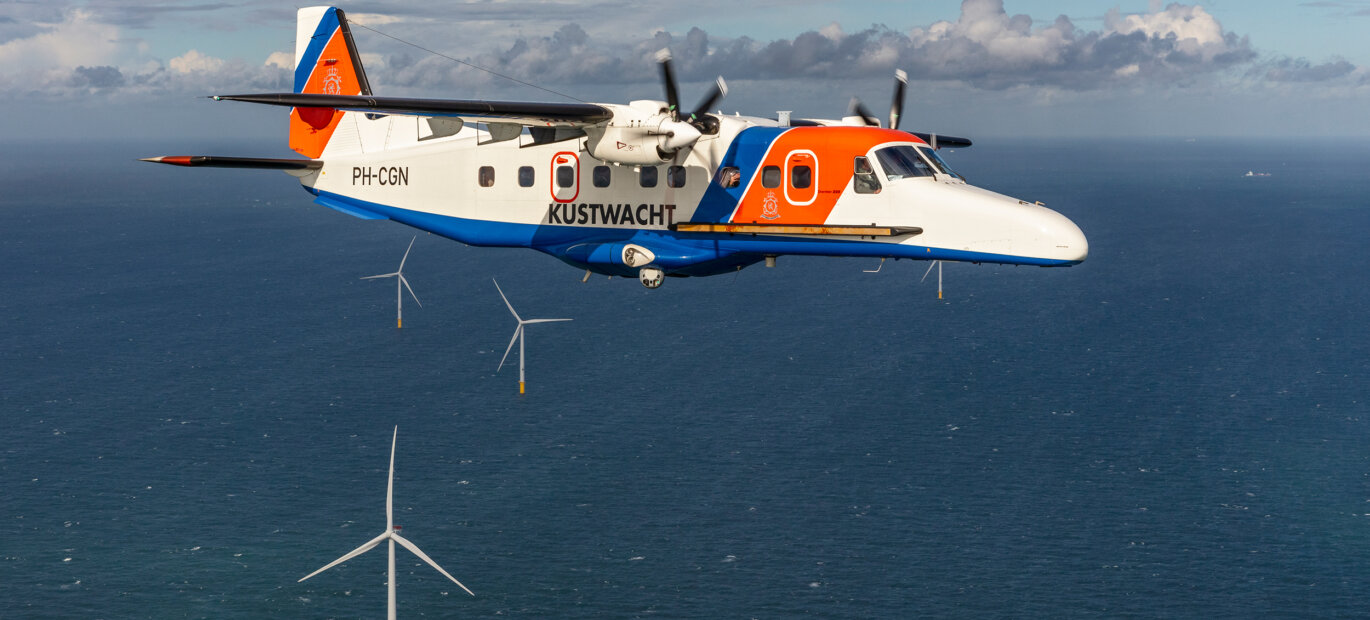 Het Kustwachtvliegtuig houdt toezicht en vliegt boven een windmolenpark op zee.