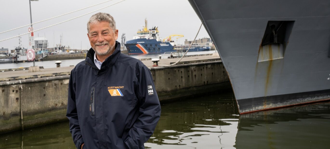 Jan van Zanten poseert in haven met een Marine- en Kustwachtschip op de achtergrond.