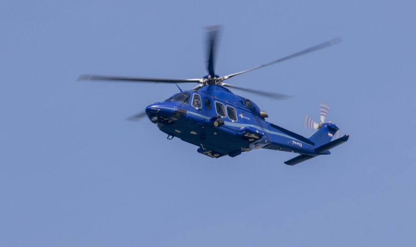 De blauwe politiehelikopter AW139 vliegt door een strak, blauwe lucht.