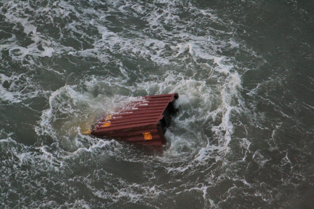 Een container drijft in zee. Een deel van de rode container is zichtbaar in het water.