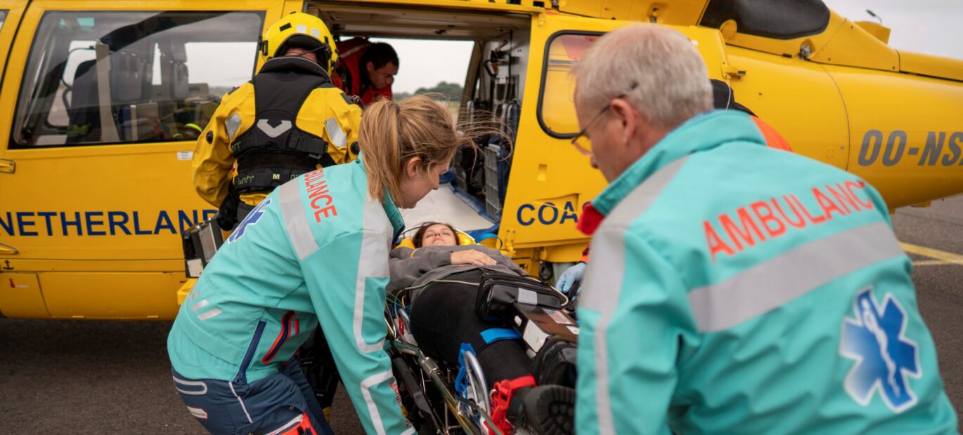 Uit de SAR-helikopter wordt voor oefening een brancard met een patiënt gehaald en overgedragen aan ambulancepersoneel.