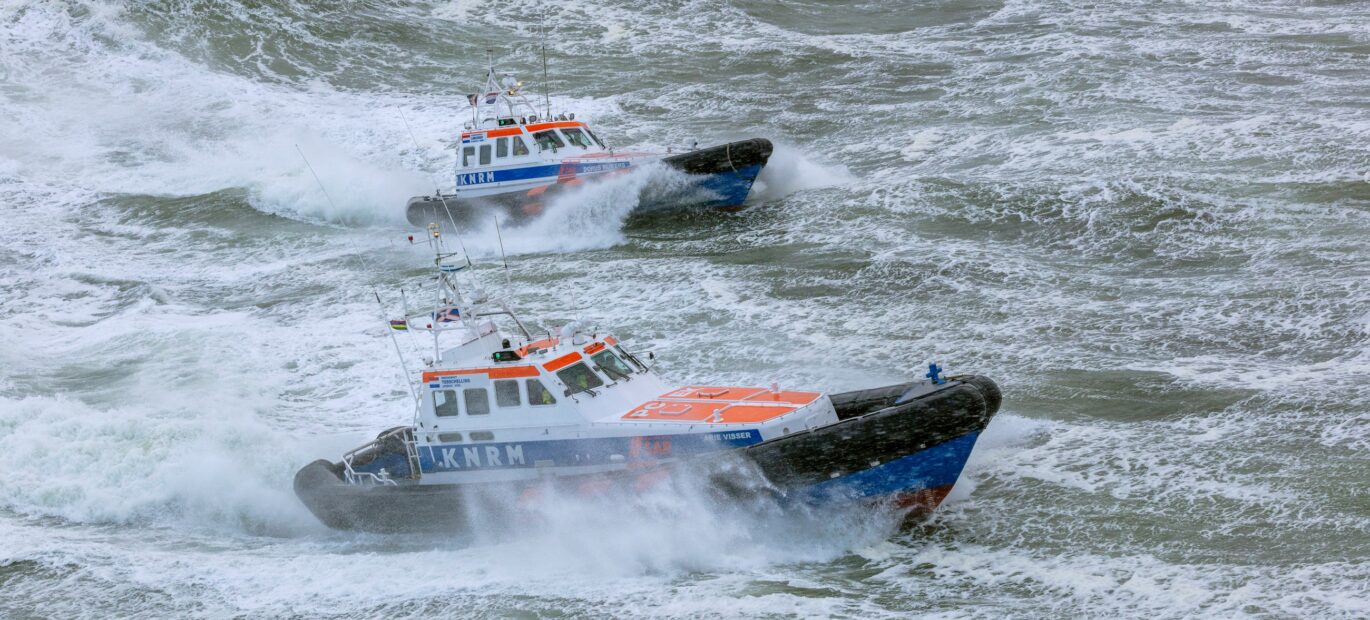 Twee grote reddingboten van de KNRM varen op een stormachtige zee.