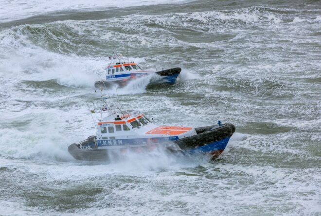 Twee grote reddingboten van de KNRM varen op een stormachtige zee.